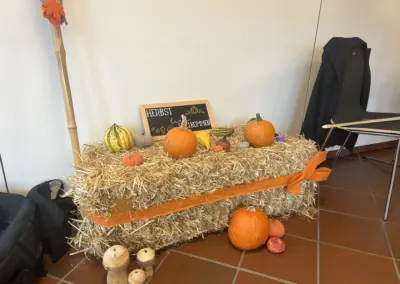 Herbstdeko mit Kürbissen auf Strohballen, orange Netzband und Schiefertafel 'Herbst willkommen'.