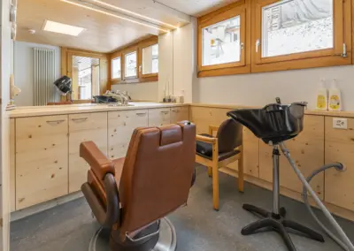 Friseursalon im Holzdesign mit Waschbecken, Ledersesseln, Spiegel und großen Fenstern; verschneite Außenansicht.