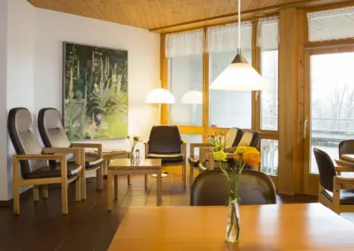 Meetingraum mit Holzdecke, großen Fenstern, Lederstühlen, Holztischen und Blumenvase.