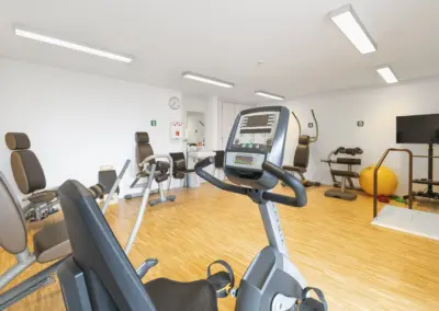 Modernes Fitnessstudio mit Cardio-Geräten: Laufbänder, Crosstrainer, Hanteln, TV-Bildschirm und Holzboden.