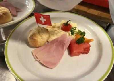 Schweizer Flagge als Dekor auf einer Vorspeisenplatte mit Schinken, Käse, Brot, Tomate und Kräutern.